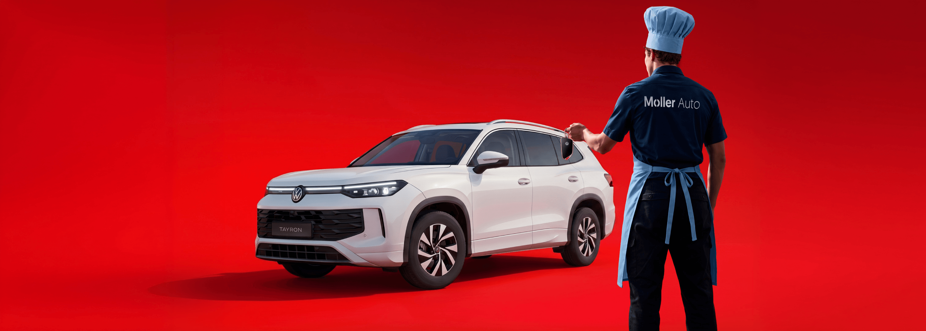 Valge Volkswagen Tayron maastur punasel taustal, kõrval Möller Auto töötaja kokamütsi ja põllega, käes auto võti.